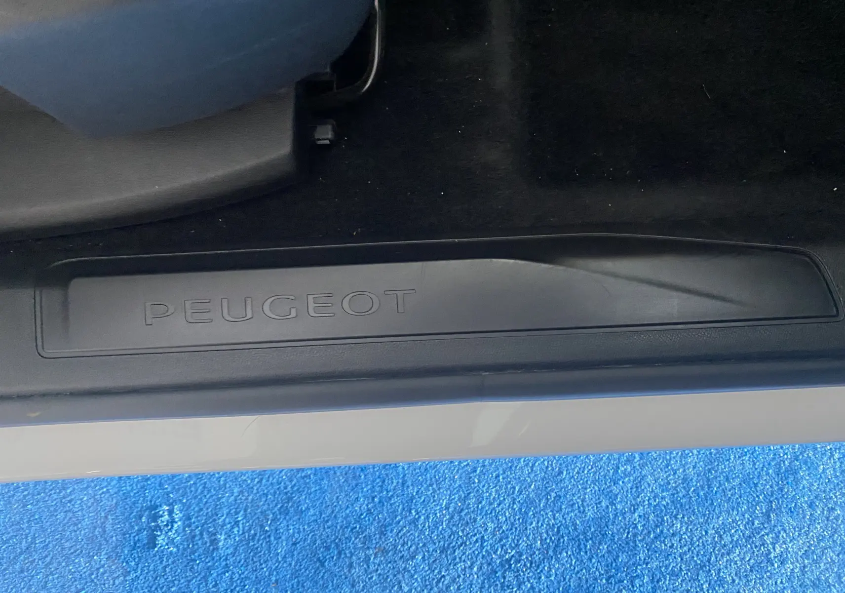 Gros plan sur la plaque de seuil de porte noire avec le logo Peugeot, sur un véhicule blanc côté gauche.