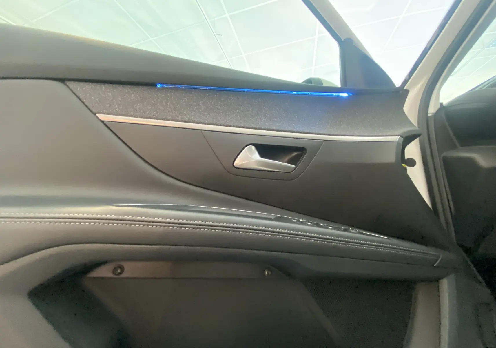 Détail de la porte avant droite du Peugeot 5008 blanc avec éclairage d'ambiance bleu et garniture noire.