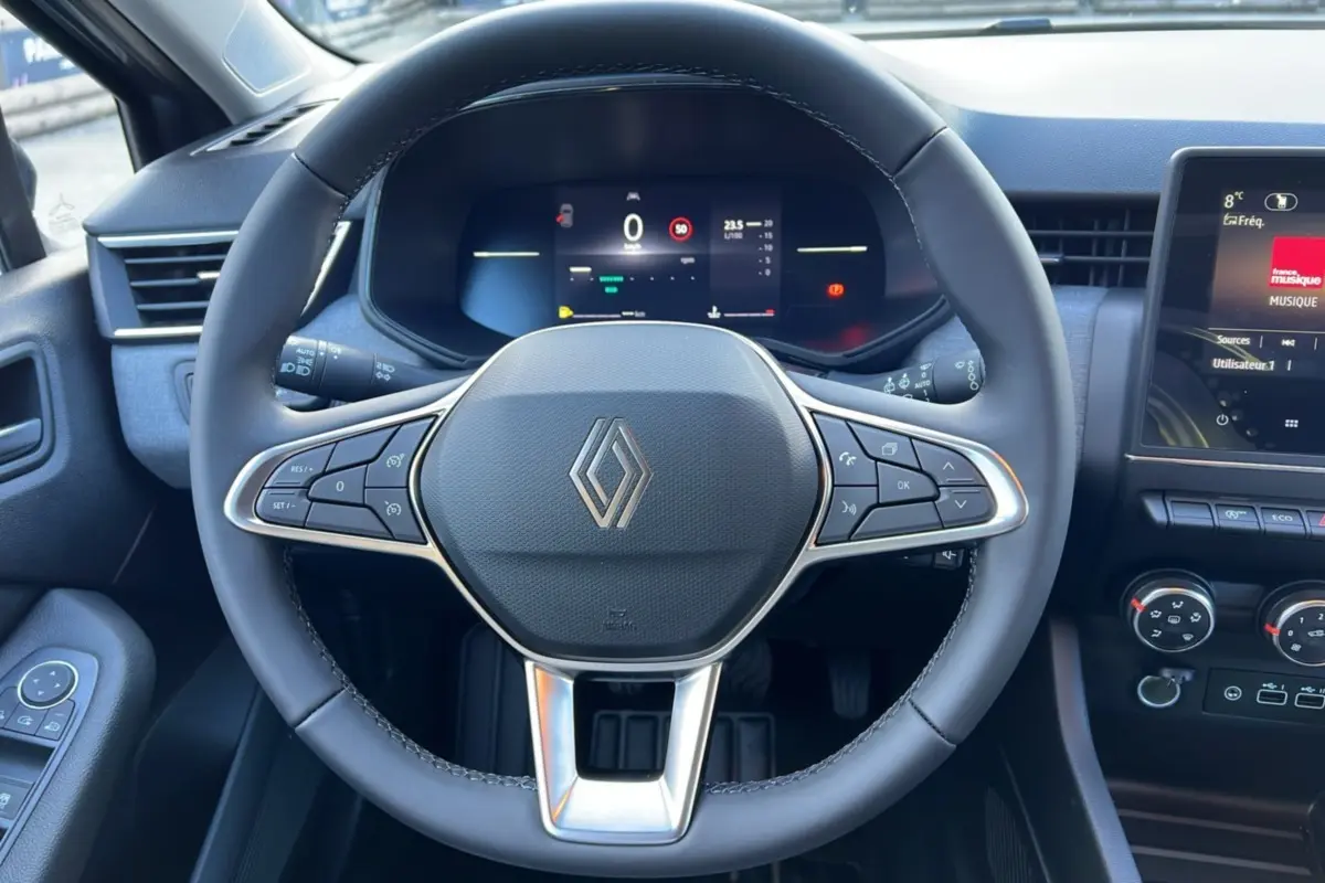 Vue intérieure centrée sur le volant du Renault Clio 2025 gris schiste avec commandes intégrées et tableau de bord digital.