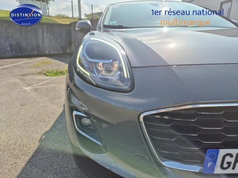 Gros plan sur l'avant gauche du Ford Puma gris métallisé avec phares LED et calandre hexagonale chrome.