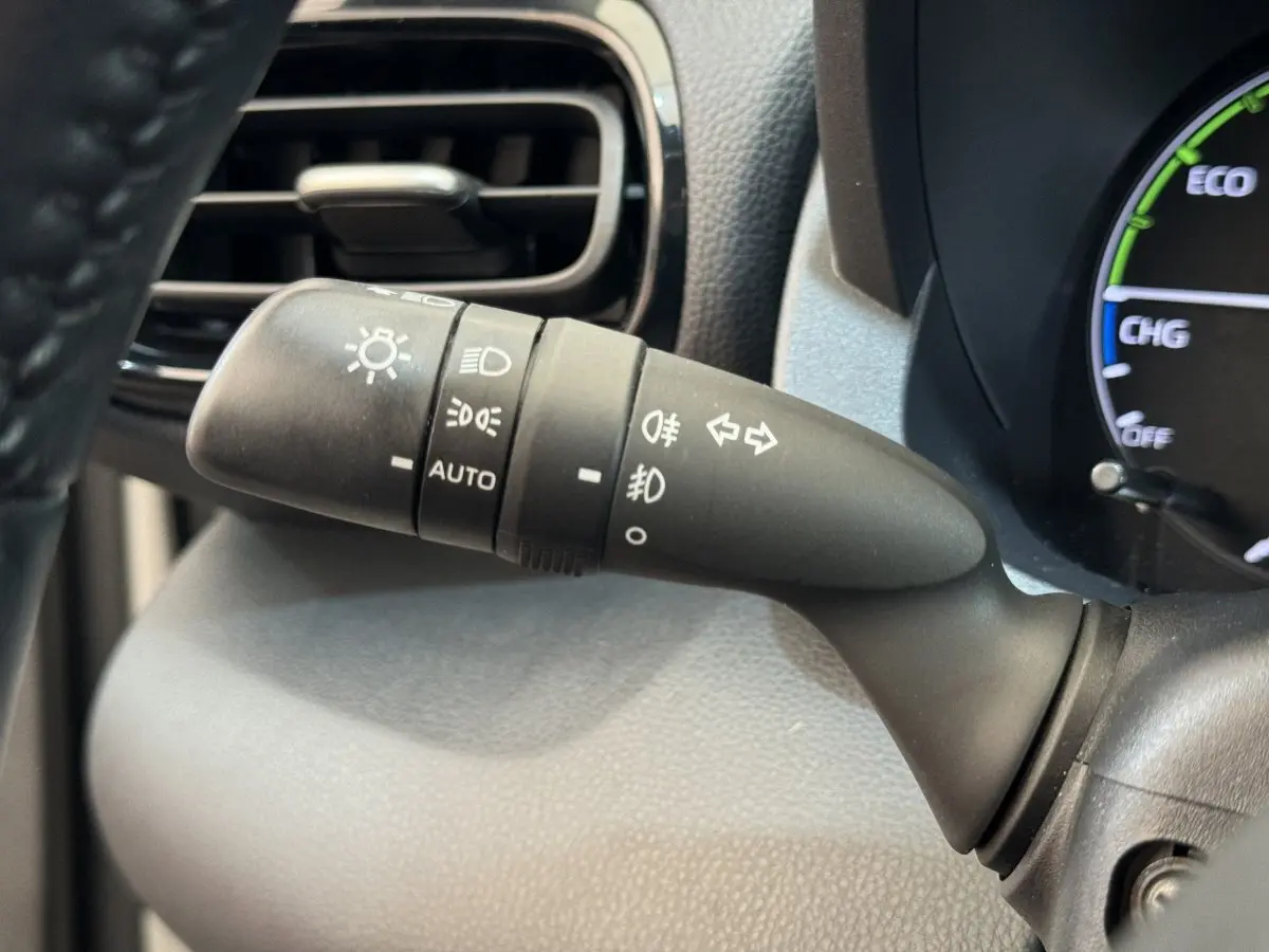 Gros plan sur la commande des phares et clignotants à gauche du volant dans l'habitacle noir de la Toyota Yaris hybride blanche.