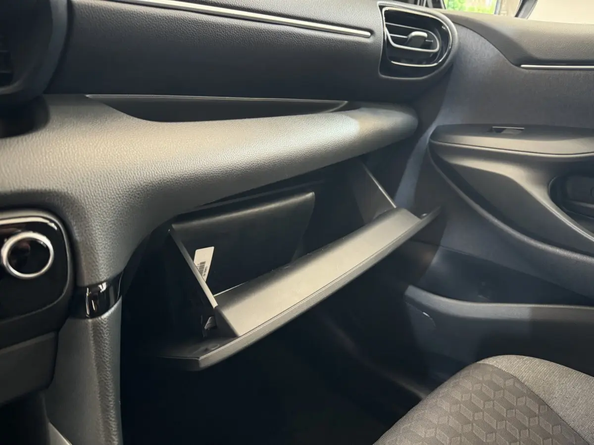 Intérieur côté passager de la Toyota Yaris hybride 2022, boîte à gants ouverte et tableau de bord noir.