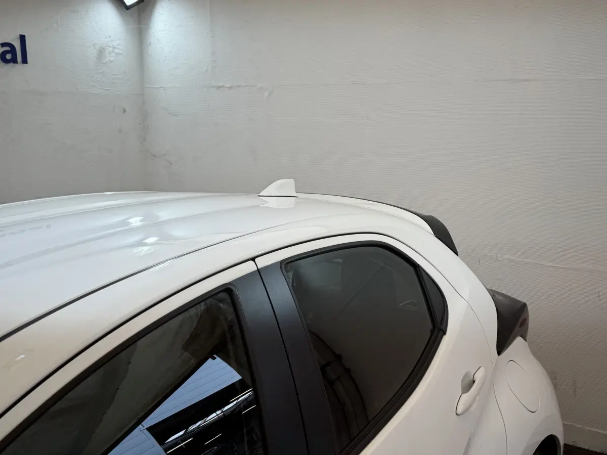 Vue latérale côté droit d'une Toyota Yaris hybride blanche avec antenne requin sur le toit et vitres teintées