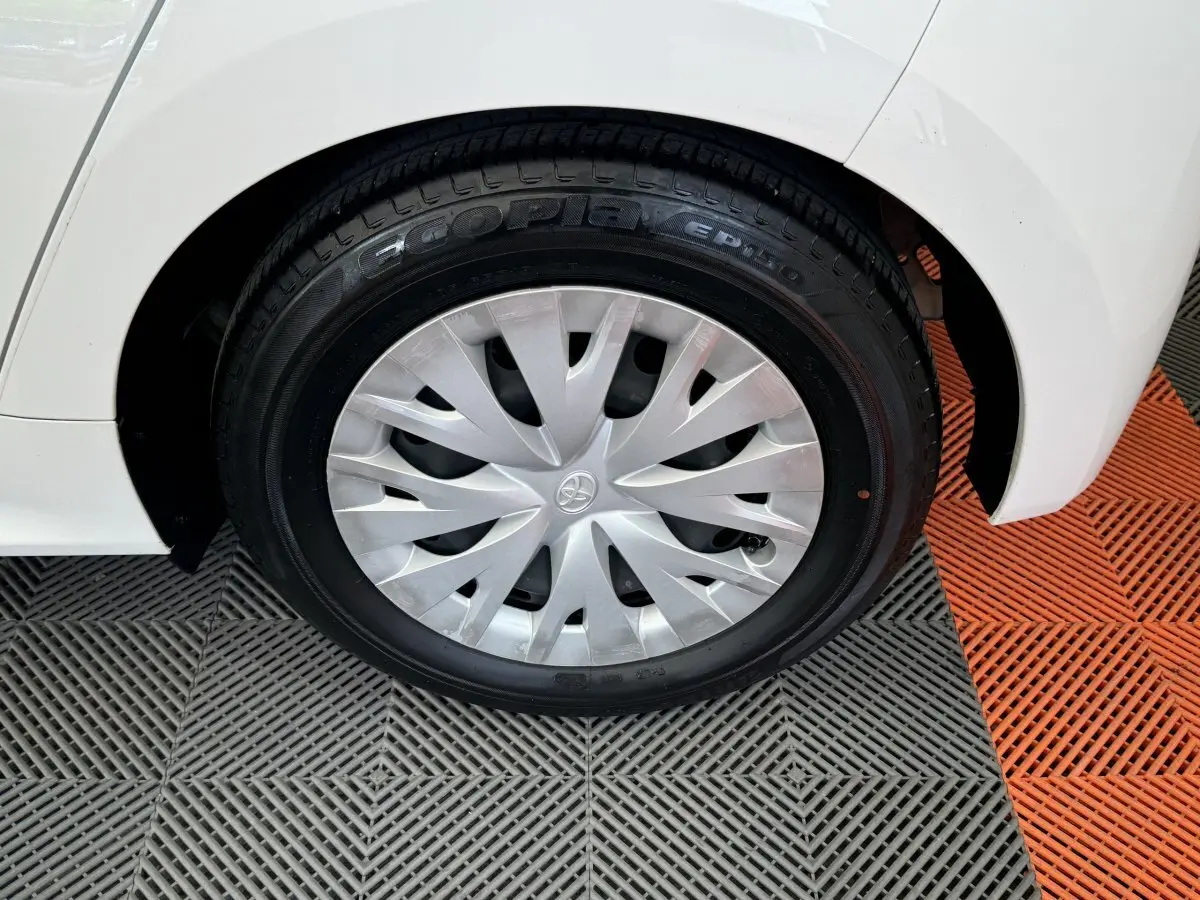 Gros plan sur la roue arrière droite blanche de la Toyota Yaris Hybride 116h avec enjoliveur argenté et logo Toyota visible.