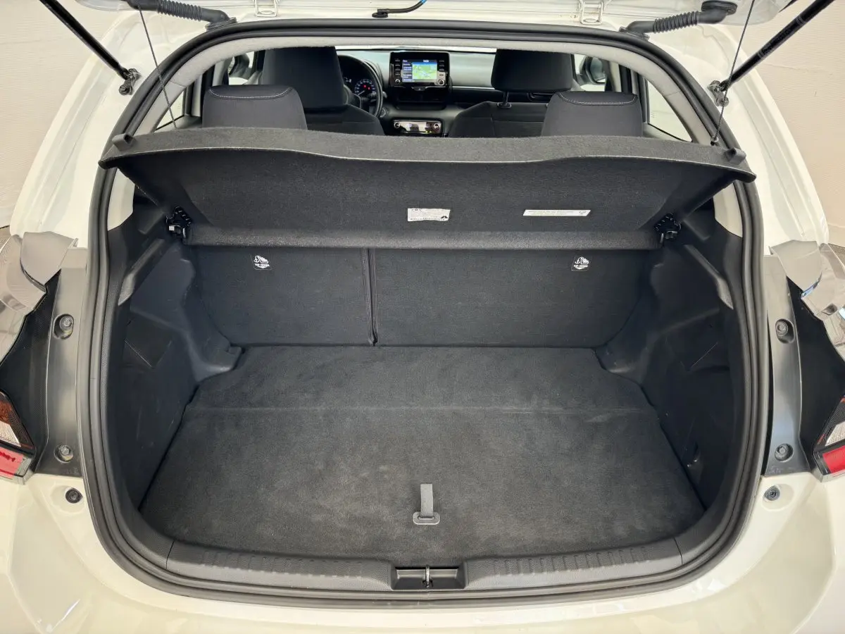 Coffre ouvert d'une Toyota Yaris blanche vue de l'arrière, avec banquette arrière et tableau de bord visible.