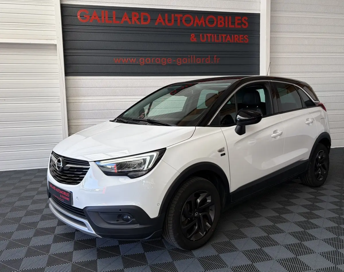Vue 3/4 avant droite d'un Opel Crossland blanc 2021 avec toit noir et jantes noires dans un showroom.