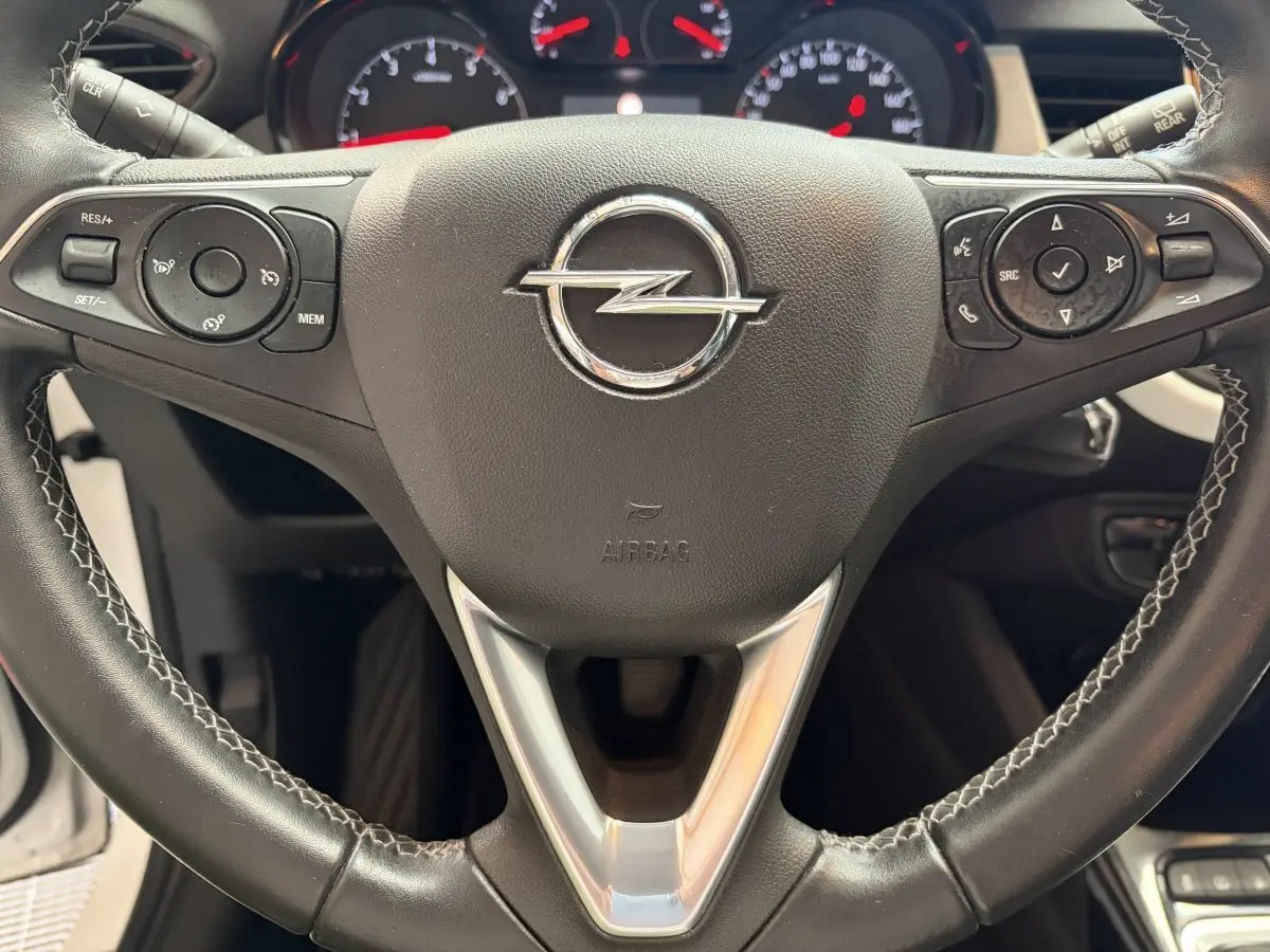 Gros plan sur le volant cuir et alu de l’Opel Crossland blanc, avec commandes multifonctions et logo central visible.