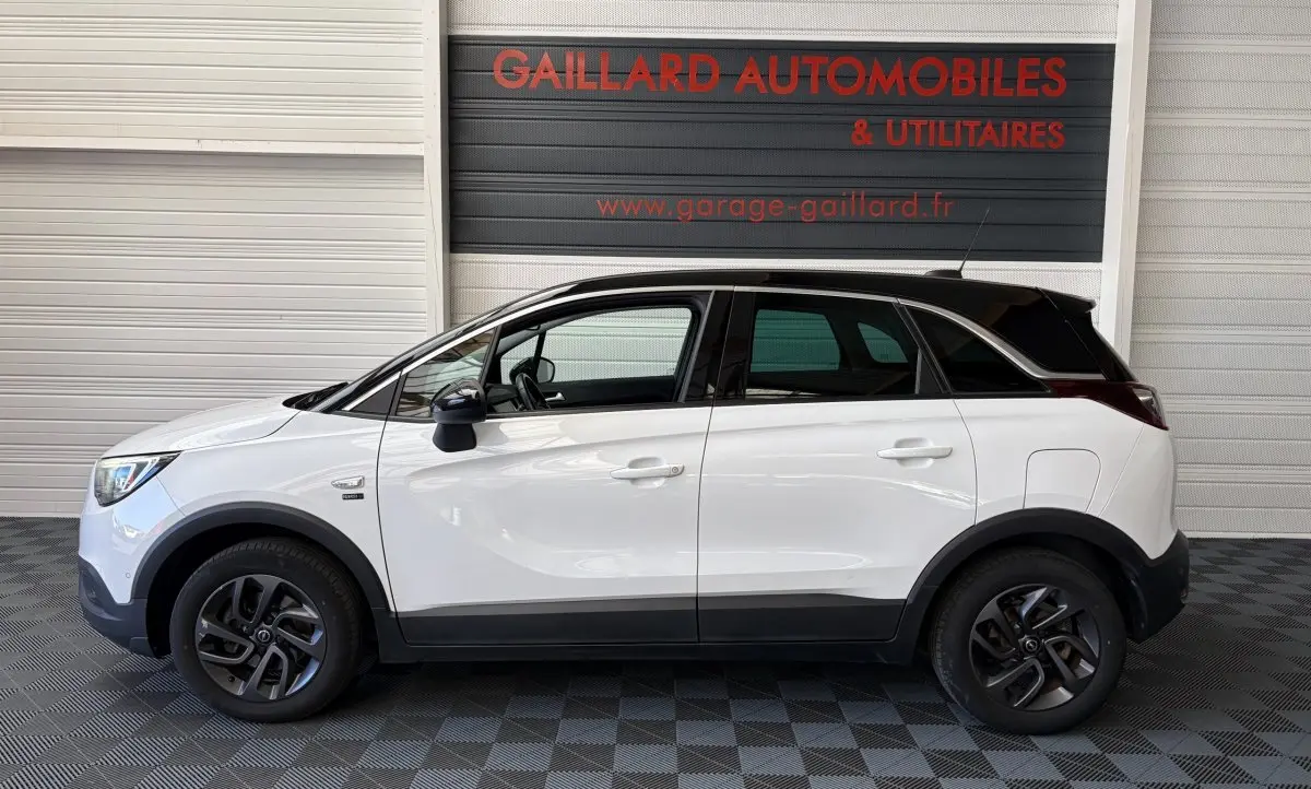 Opel Crossland blanc vue de profil côté gauche, toit noir contrasté et jantes foncées, en intérieur de garage.