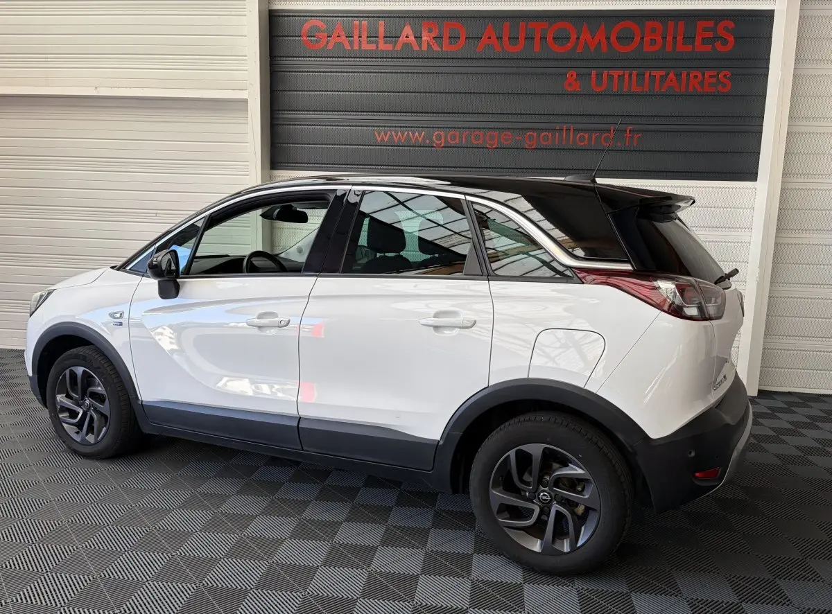 Vue de profil côté gauche d'un Opel Crossland blanc avec toit noir et jantes foncées dans un garage.