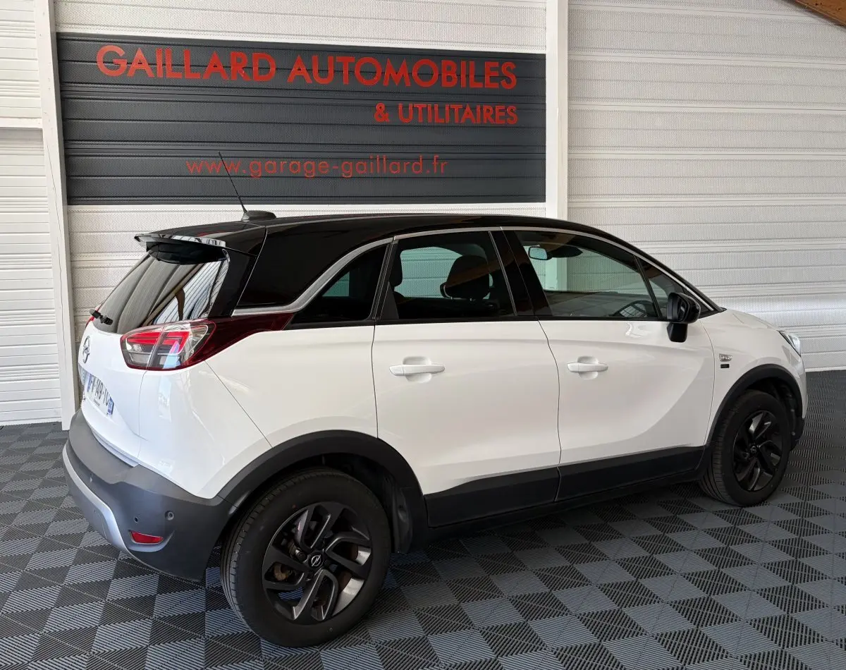 Vue 3/4 arrière droite de l’Opel Crossland blanc avec toit noir et jantes noires dans un garage.