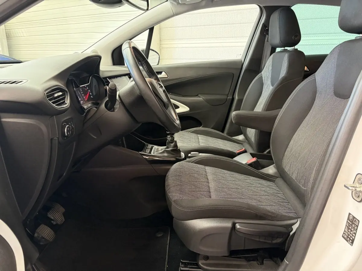 Vue intérieure côté conducteur de l’Opel Crossland blanc, montrant les sièges tissu et le volant multifonctions cuir.