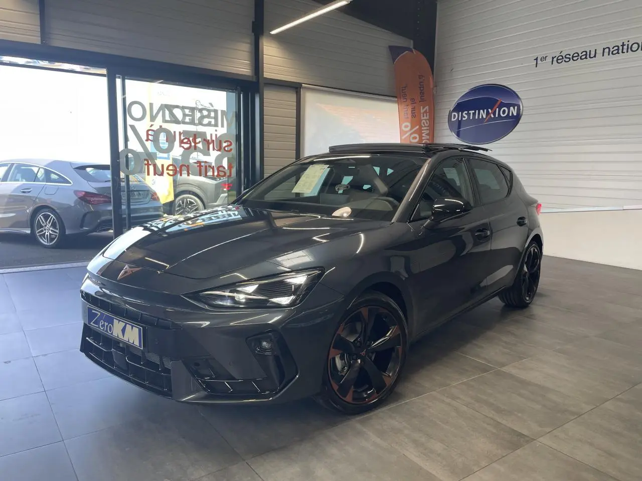 Vue 3/4 avant d'une CUPRA Leon gris magnetic avec jantes cuivrées et toit ouvrant panoramique en showroom.