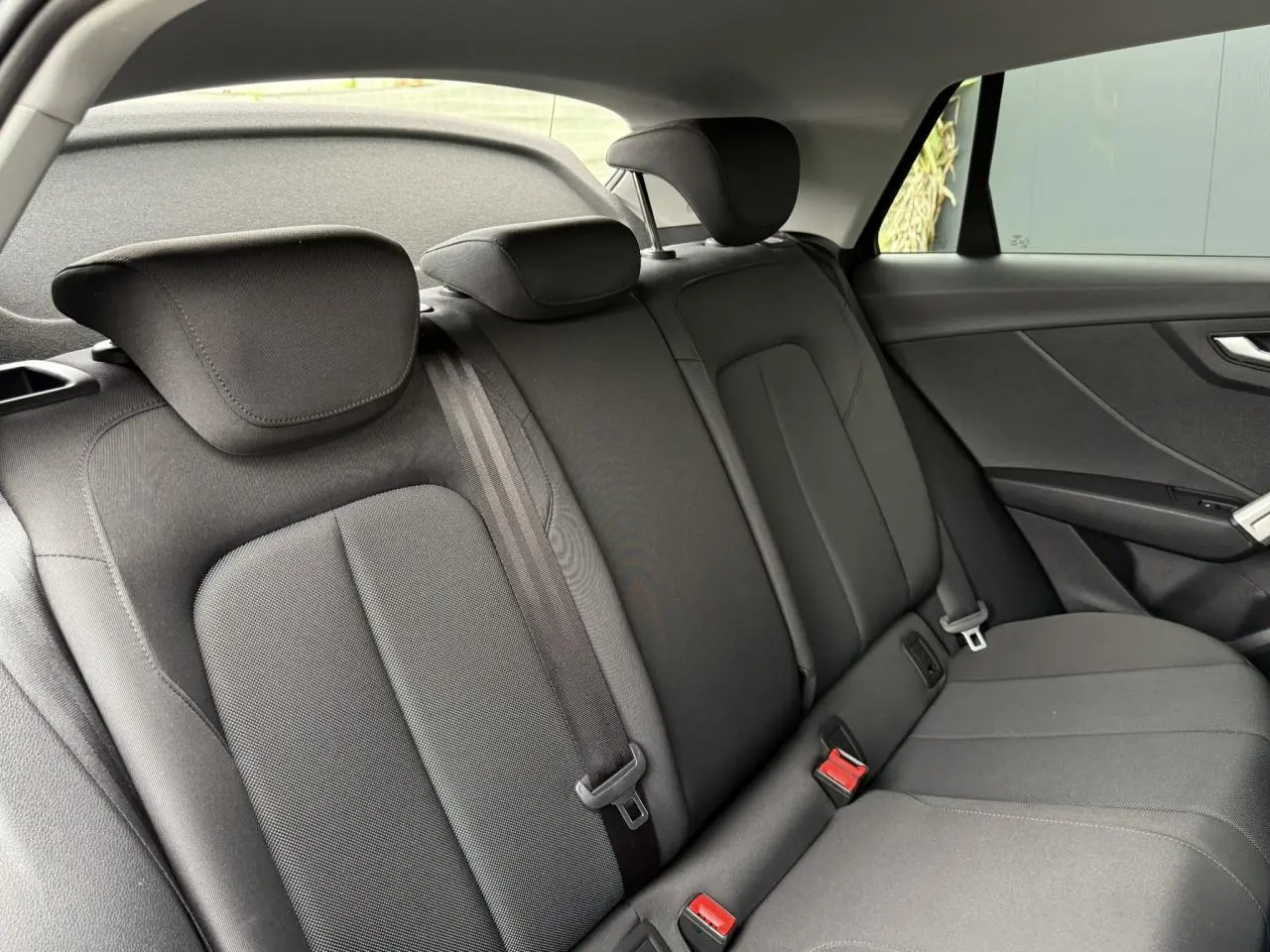 Vue intérieure montrant la banquette arrière noire de l'Audi Q2 35 TFSI S-Line, avec appuie-têtes et ceintures de sécurité.