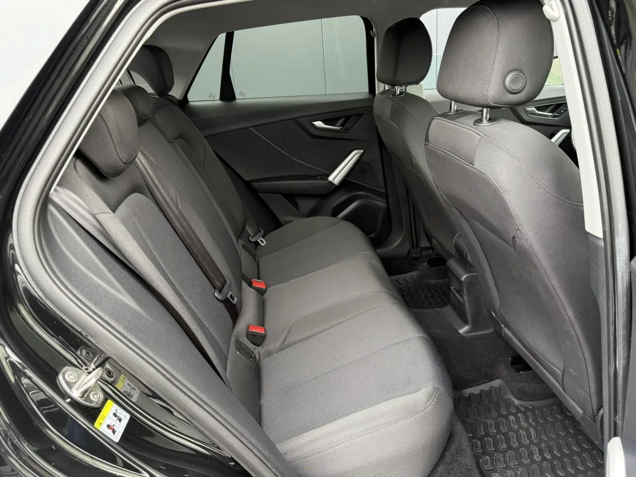 Vue intérieure côté gauche des sièges arrière gris foncé d'un Audi Q2 noir Mythe 2023 avec portes ouvertes.