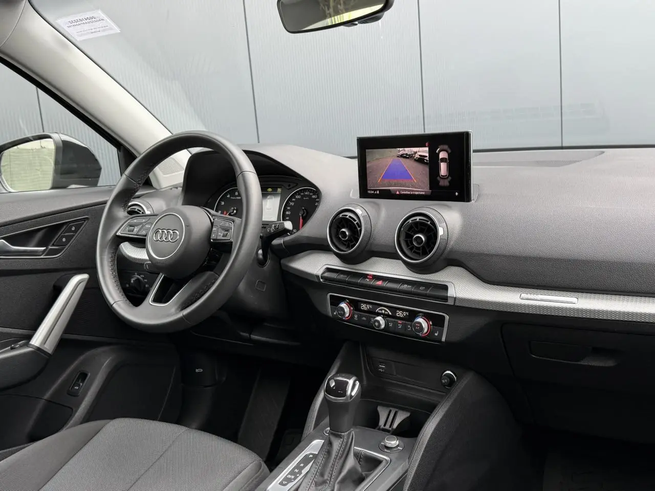 Intérieur de l'Audi Q2 35 TFSI 2023 vu côté conducteur, tableau de bord avec écran caméra de recul et climatisation automatique.