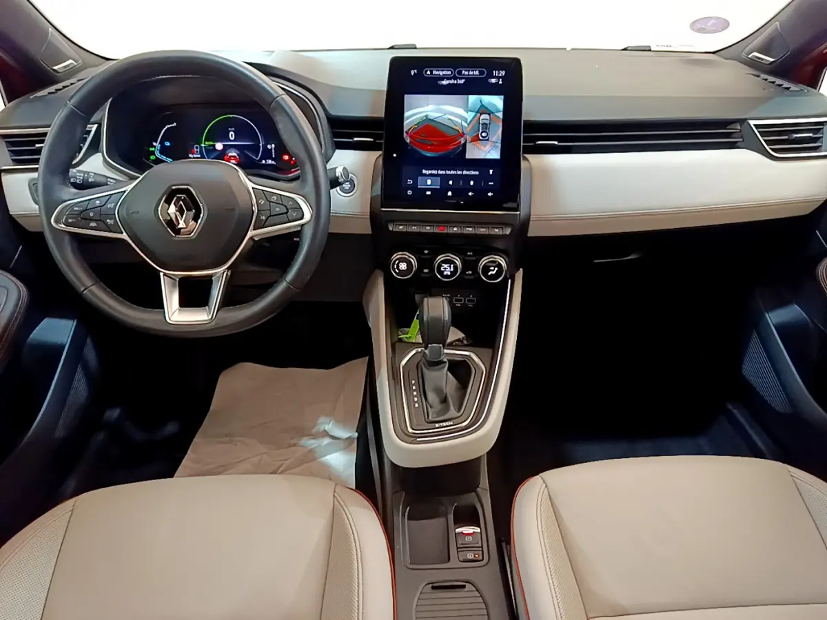 Vue intérieure avant du tableau de bord beige et noir de la Renault Clio Initiale Paris E-TECH 140 avec écran tactile central et volant cuir.
