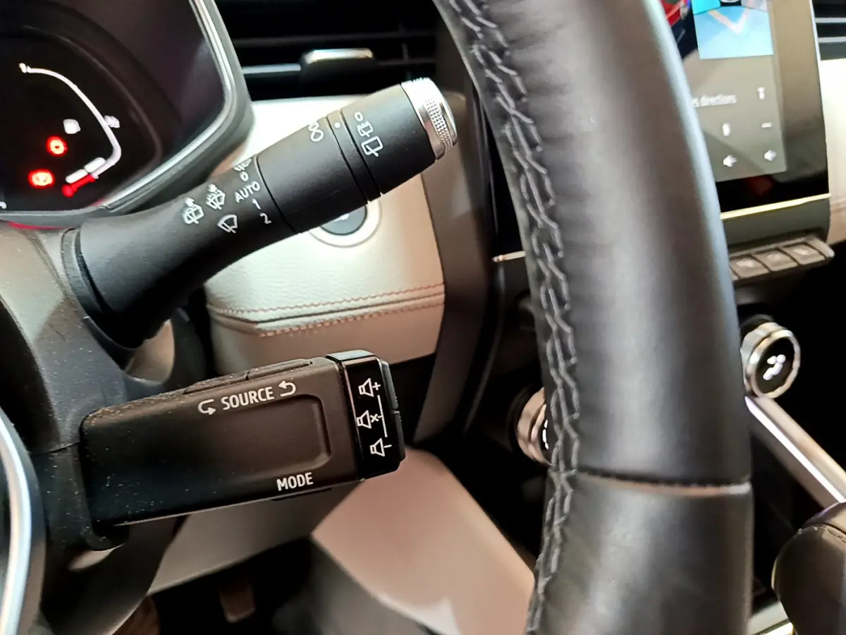 Vue rapprochée du volant noir et des commandes multimédia sur la gauche dans l'habitacle beige d'une Renault Clio orange.