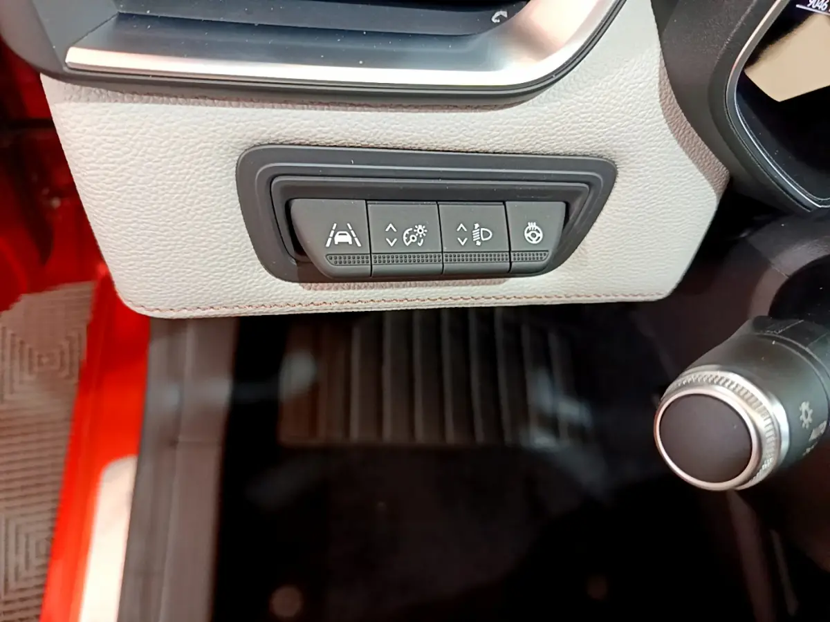 Gros plan sur les commandes d'assistance et éclairage sous le tableau de bord beige d'une Renault Clio Initiale Paris orange.