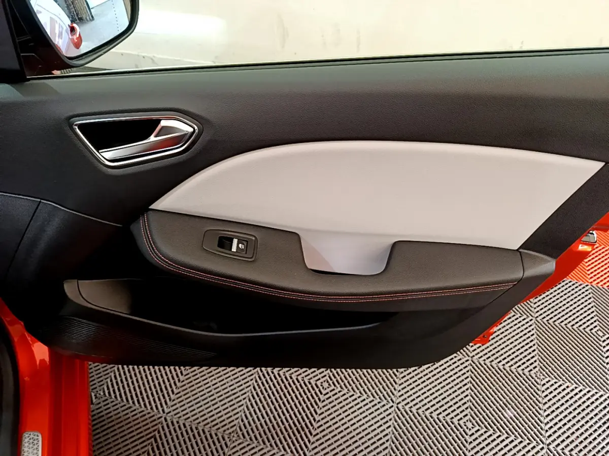 Gros plan sur la porte côté gauche de la Renault Clio Initiale Paris orange, avec garniture bicolore et bouton de vitre électrique.