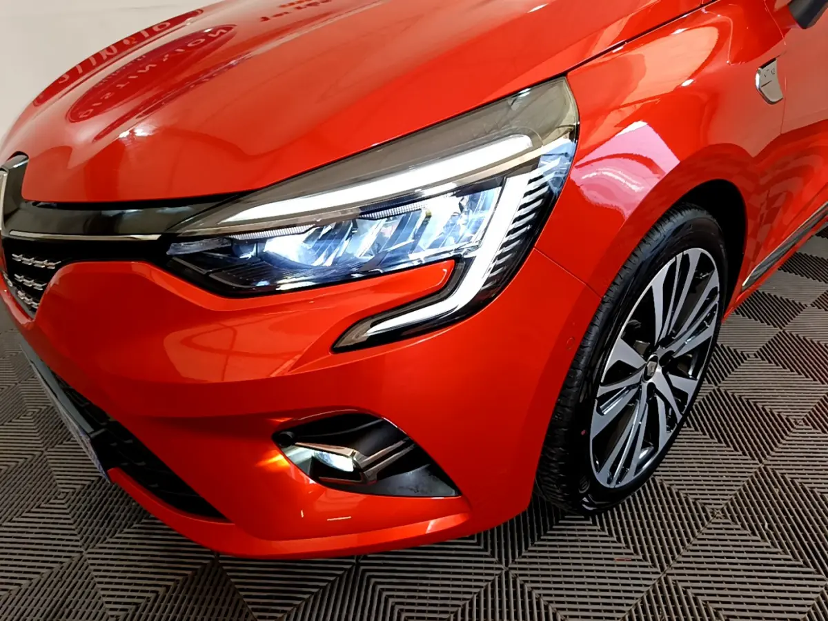 Gros plan sur l'avant droit orange vif de la Renault Clio Initiale Paris 2021, mettant en valeur le phare LED et la jante stylée.