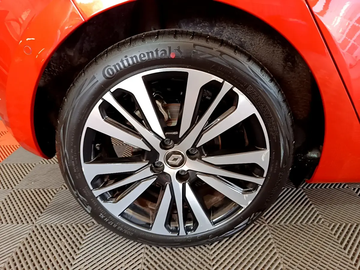 Gros plan sur la roue avant droite orange d'une Renault Clio Initiale Paris E-TECH 140 avec jante alliage bicolore.