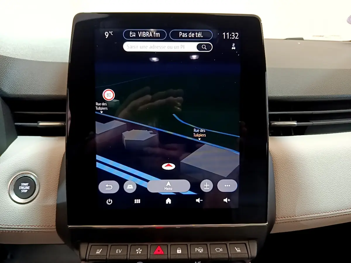 Écran tactile central affichant la navigation dans l'habitacle beige d'une Renault Clio Initiale Paris orange, bouton démarrage visible.