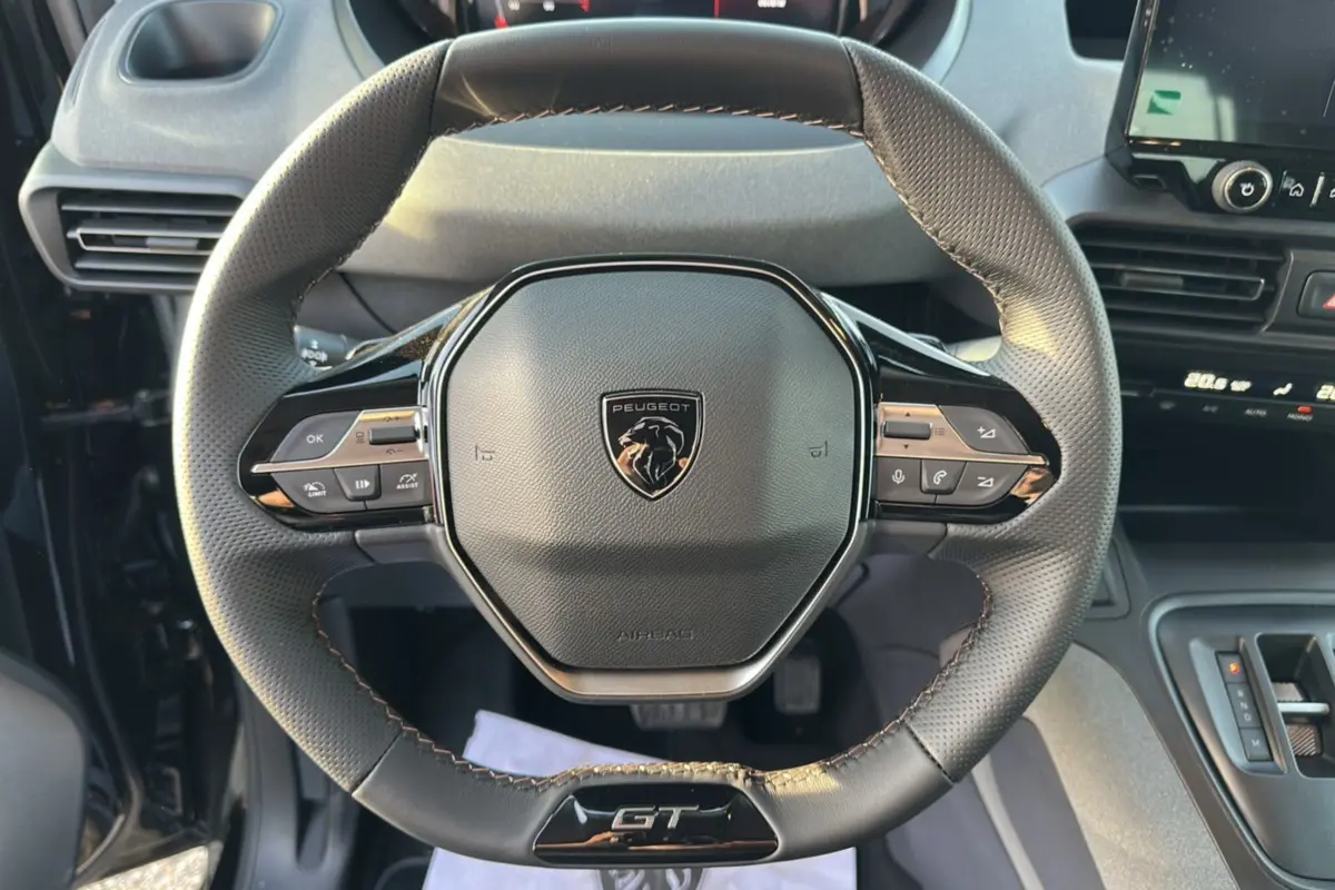 Vue rapprochée du volant cuir multifonctions Peugeot Rifter GT Plus noir avec logo central et commandes intégrées.