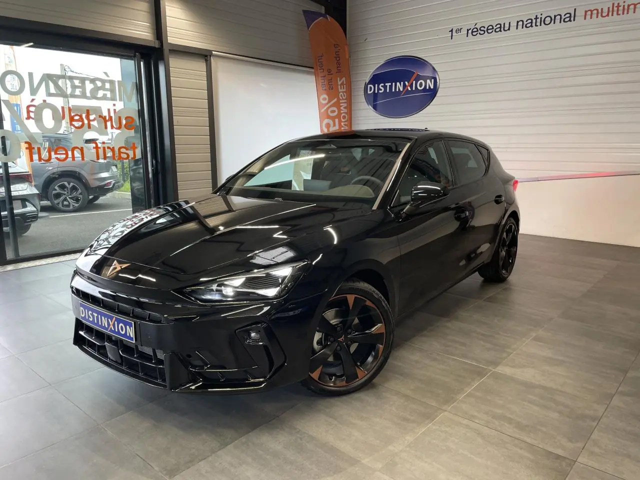 Vue 3/4 avant droite d'une CUPRA Leon noire avec jantes alliage noires et cuivrées, dans un showroom intérieur.