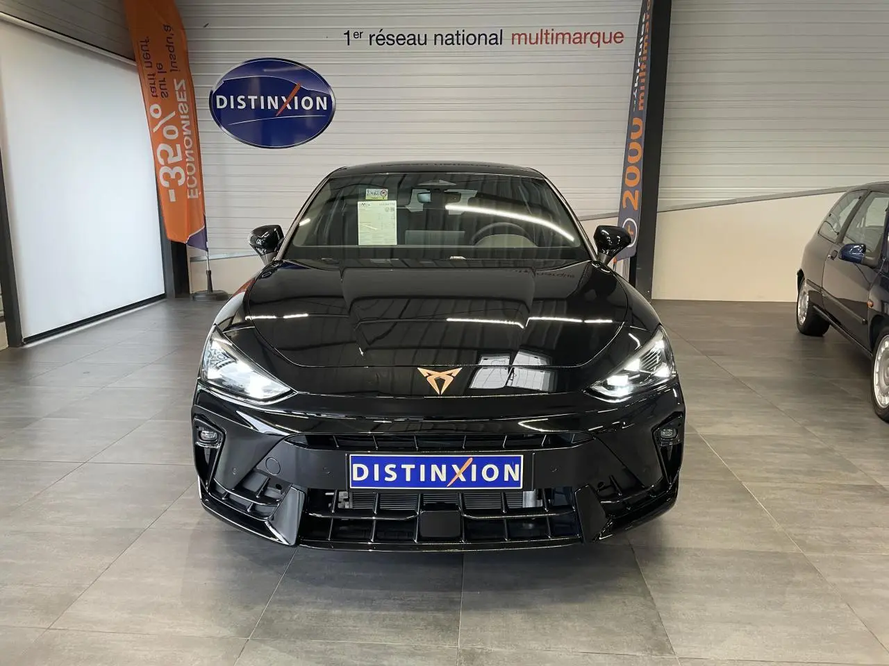 Vue de face d'une CUPRA Leon noire avec logo cuivré, phares allumés et calandre sportive en showroom.