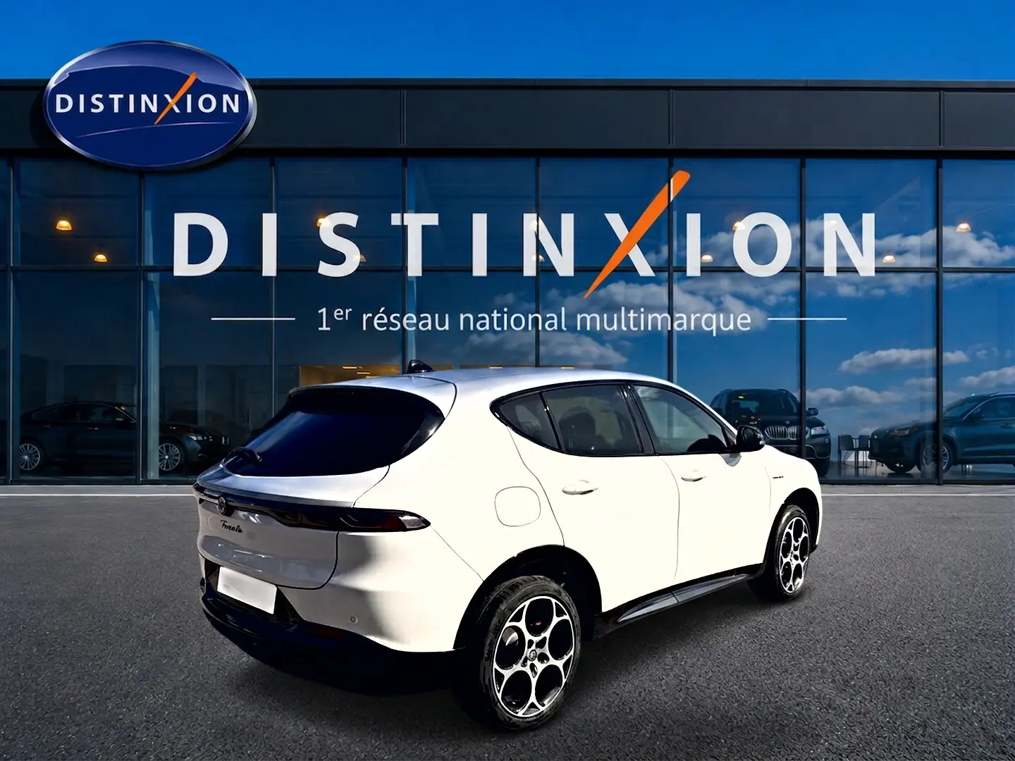 Vue 3/4 arrière droite d'un Alfa Romeo Tonale blanc avec jantes alu et vitres arrière surteintées devant un showroom Distinxion.