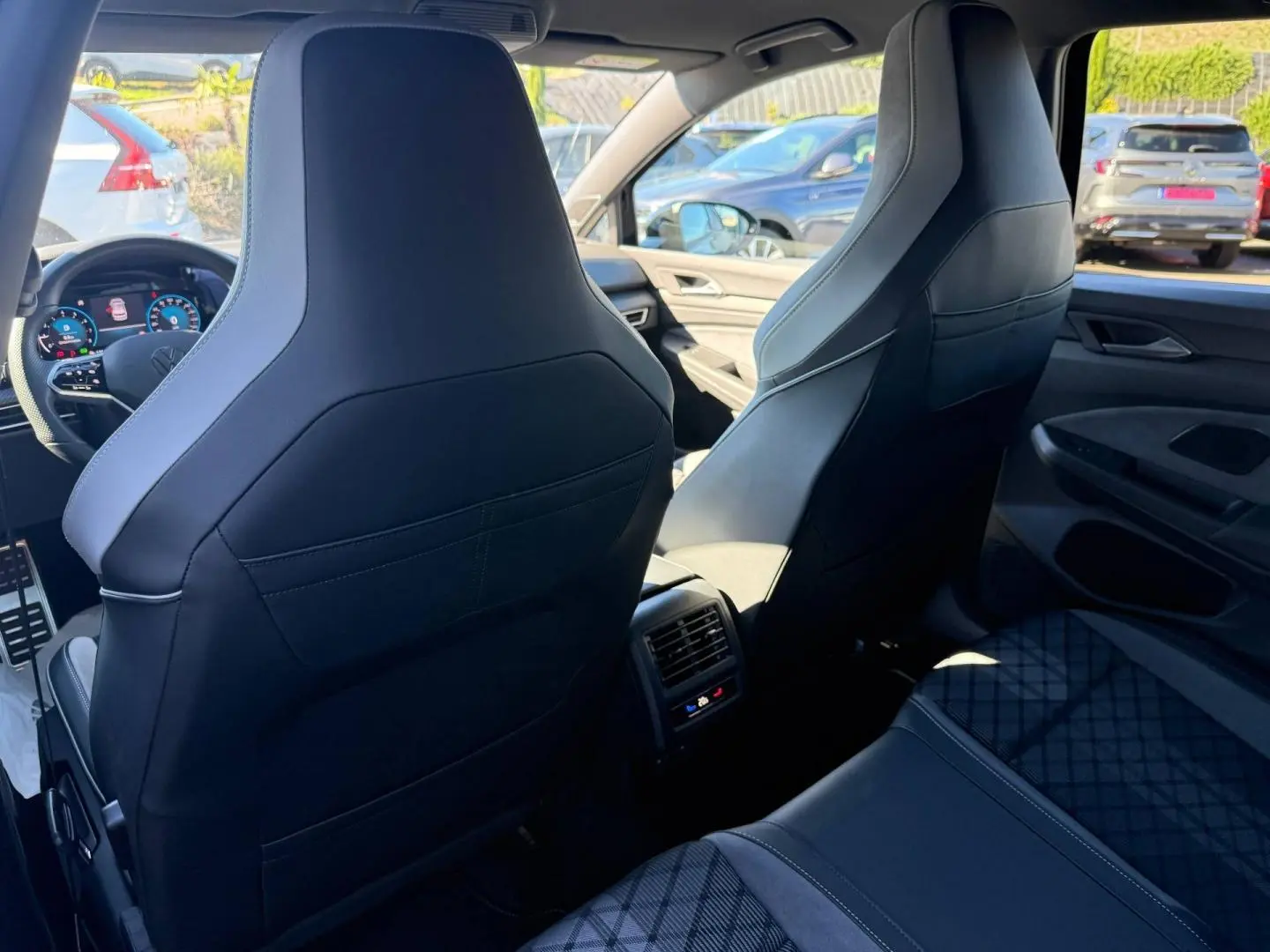 Vue intérieure arrière de la Volkswagen Golf 1.5 eTSI R-Line 2024 avec sièges sport noirs et console centrale avec aérateurs.