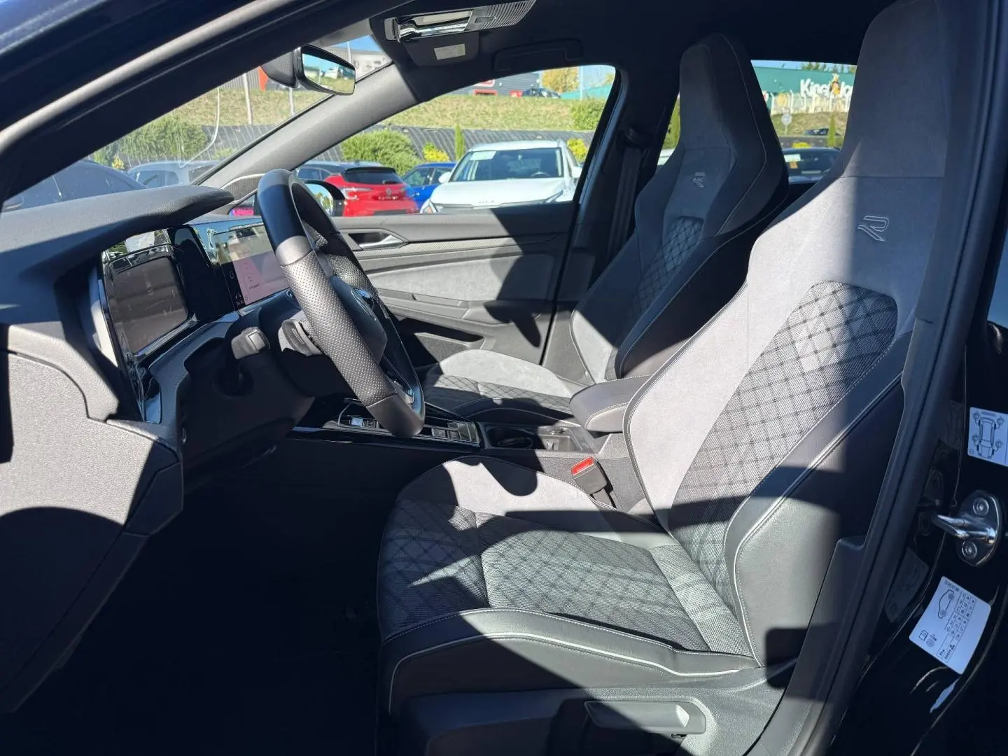 Vue intérieure côté conducteur de la Volkswagen Golf 1.5 eTSI R-Line 2024 avec sièges sport en tissu gris et volant cuir multifonction.