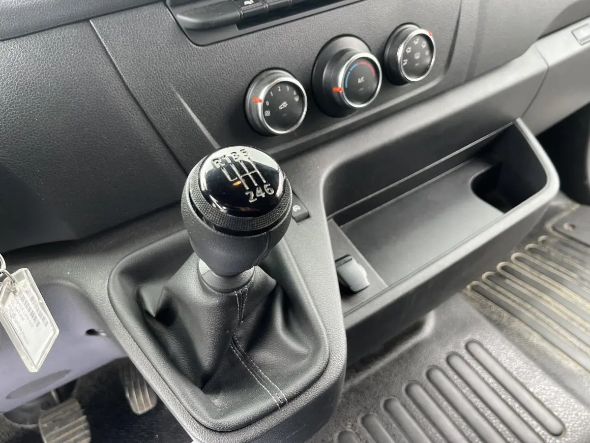 Gros plan sur le levier de vitesses manuel noir et la console centrale du Renault Master blanc, avec commandes de climatisation visibles.
