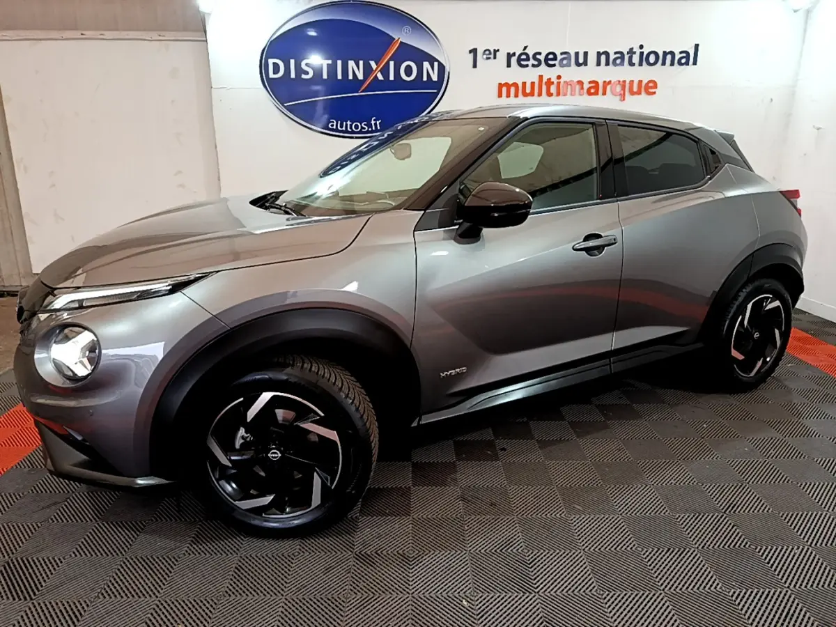 Nissan Juke Hybrid gris foncé vue de profil côté gauche, avec jantes noires et logo Distinxion en arrière-plan.
