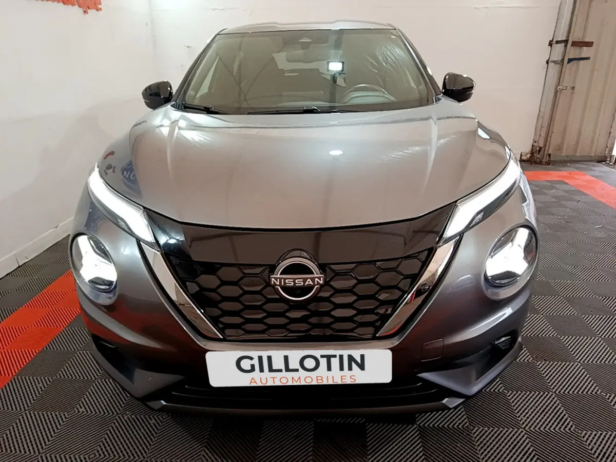 Vue frontale d'un Nissan Juke Hybrid 143 Business+ gris foncé avec phares allumés et calandre noire hexagonale.