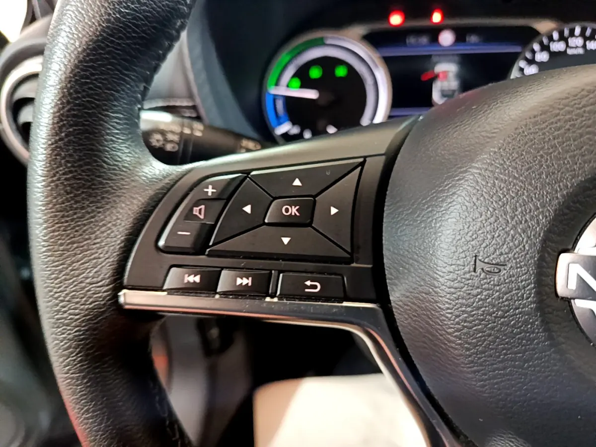 Gros plan sur le volant cuir noir à commandes multifonctions du Nissan Juke Hybrid 143 Business+ gris foncé, tableau de bord en arrière-plan.