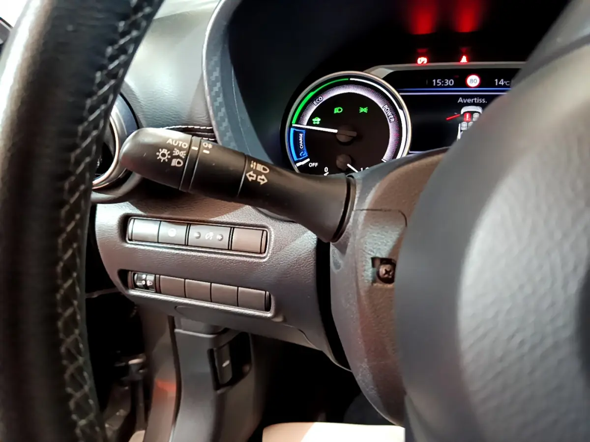 Gros plan sur le combiné d'instruments et la commande des phares à gauche du volant du Nissan Juke Hybrid gris foncé 2023.