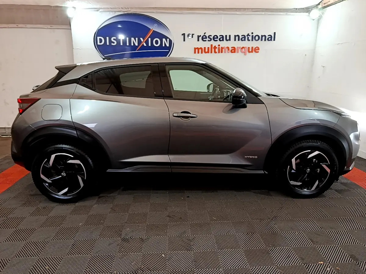 Profil côté gauche du Nissan Juke Hybrid 143 Business+ gris foncé avec jantes noires et logo hybrid visible.