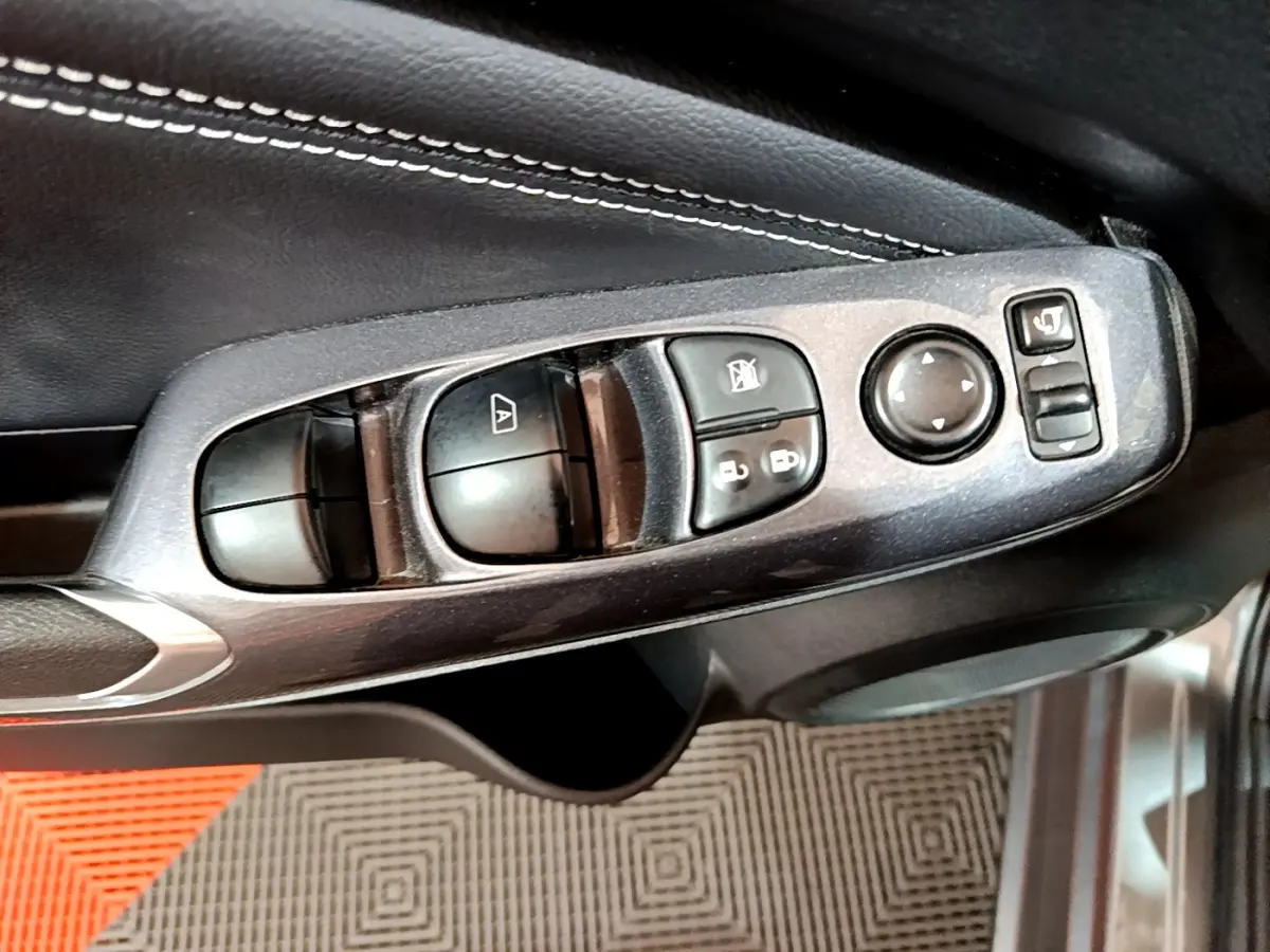 Gros plan sur les commandes de lève-vitres et rétroviseurs côté conducteur du Nissan Juke Hybrid gris foncé 2023.