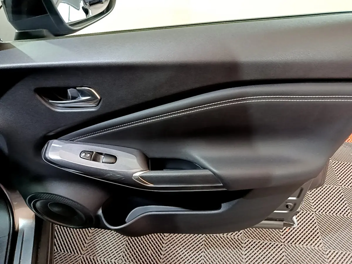 Gros plan sur la porte côté gauche intérieure du Nissan Juke Hybrid gris foncé avec commandes de vitres et haut-parleur.
