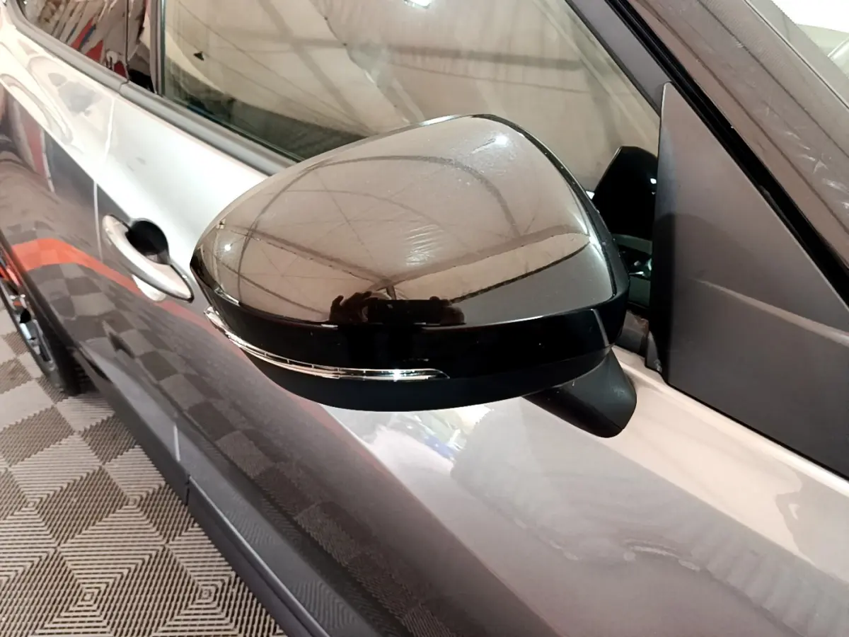 Rétroviseur noir brillant côté gauche du Nissan Juke Hybrid gris foncé 2023 avec clignotant intégré visible.