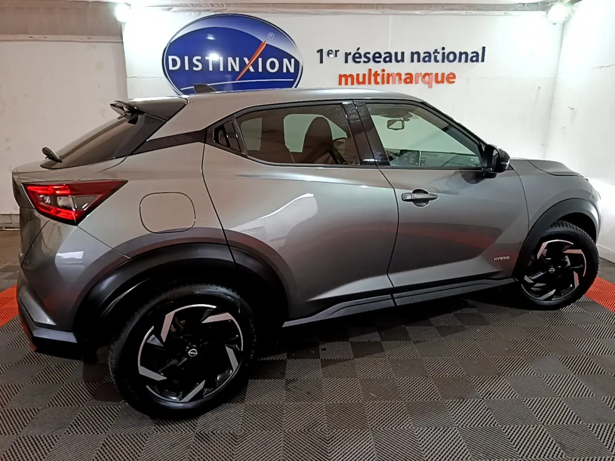 Profil droit du Nissan Juke Hybrid 143 Business+ gris foncé avec jantes noires et toit noir en intérieur showroom.