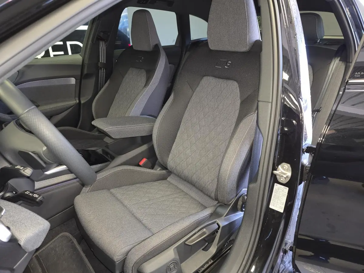 Vue intérieure côté conducteur d'une Audi A5 Avant 2025 noire, sièges sport S line en tissu gris avec surpiqûres beige.