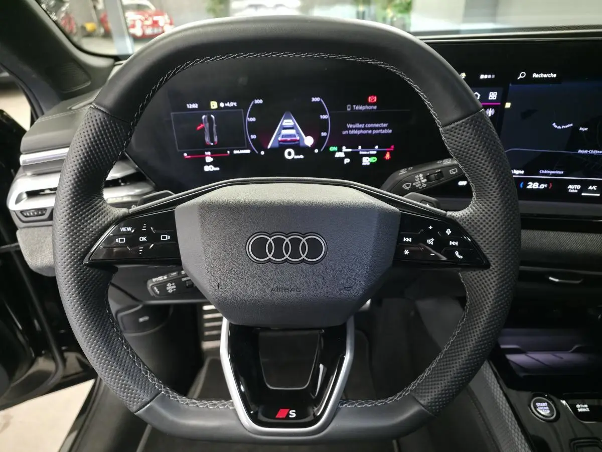 Volant sport en cuir avec logo Audi et S, vue frontale du poste de conduite numérique de l'Audi A5 Avant noir 2025.