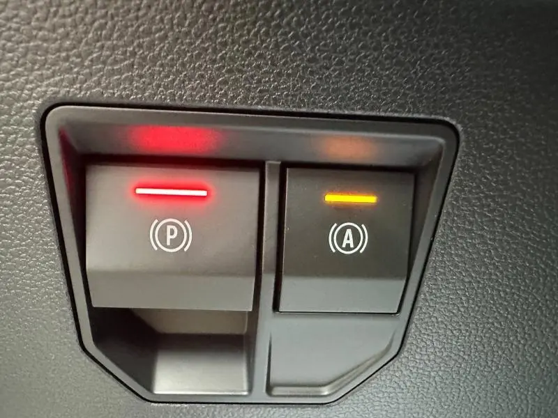 Gros plan sur les boutons de frein à main électronique et d'assistance au démarrage du Renault Scénic rouge.