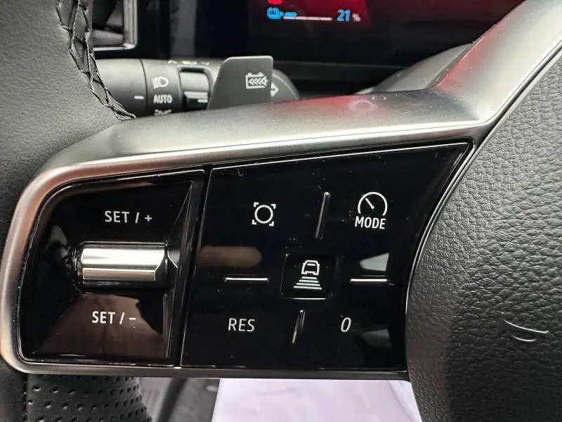 Gros plan sur les commandes noires du volant multifonction du Renault Scénic E-Tech rouge, avec boutons de régulateur et mode de conduite.