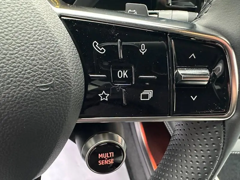 Gros plan sur les commandes noires du volant à droite du Renault Scénic rouge, avec bouton Multi Sense visible dessous.