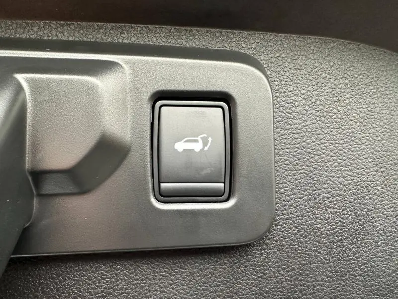 Gros plan sur le bouton noir d'ouverture électrique du coffre dans l'habitacle du Renault Scénic rouge 2025.