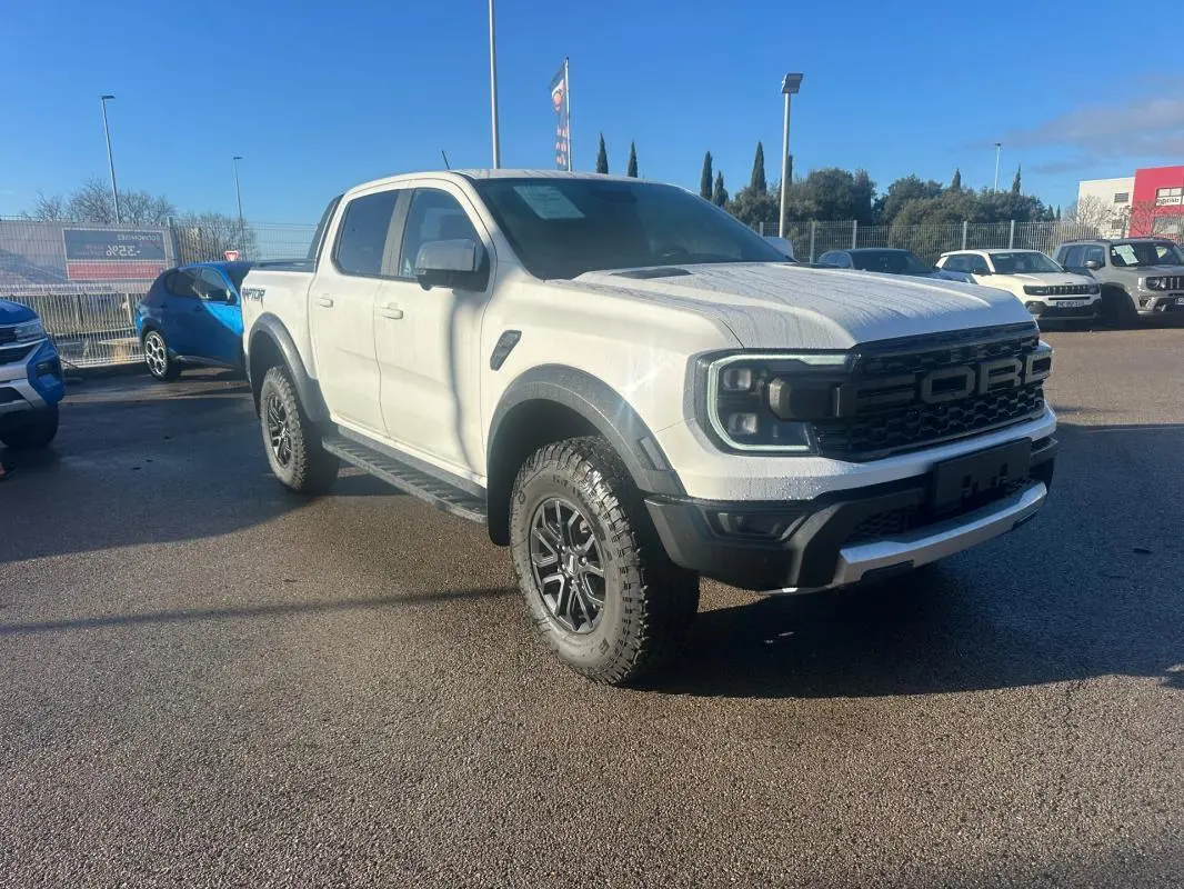 Ford Ranger Raptor blanc en 3/4 avant droit avec jantes alliage noires et marchepieds visibles sur parking.