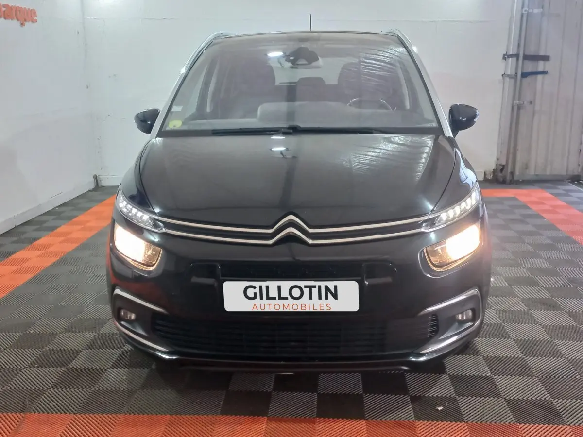 Vue frontale d'un Citroën Grand C4 Spacetourer noir avec phares allumés dans un garage.
